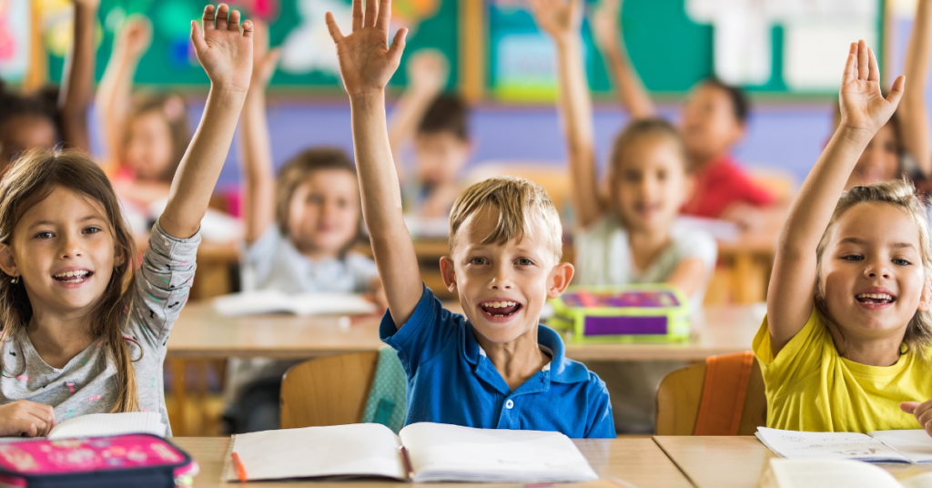 a classroom of mostly white kids all raise their hands