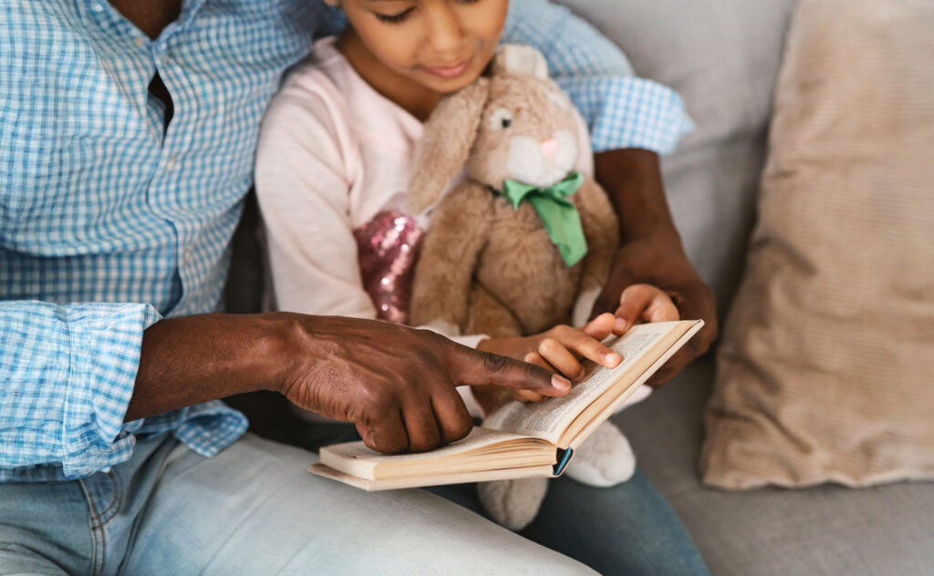 Close-up of a parent and child’s hands holding a book open together, showing a shared reading moment